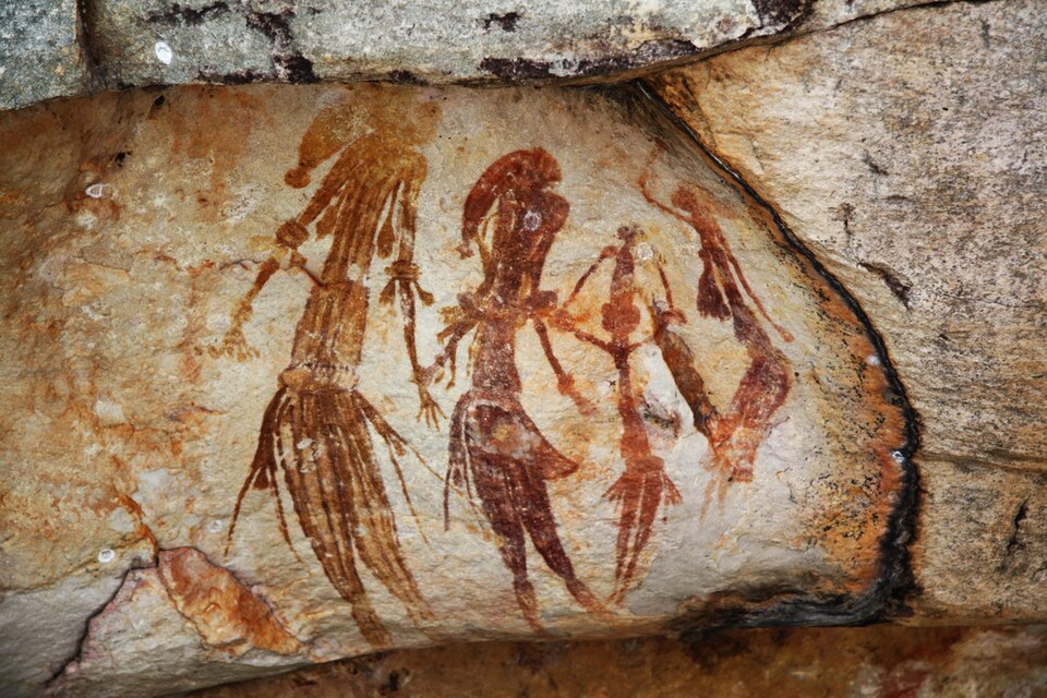 Ochre human figures painted on a rough stone surface.