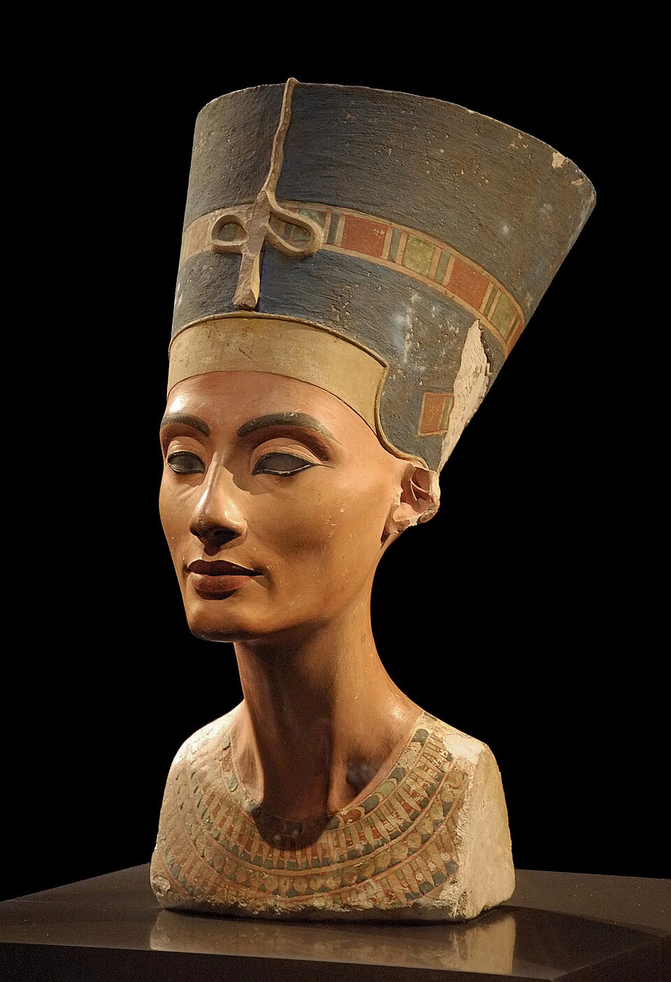A painted bust of Nefertiti wearing a tall blue crown, photographed against a neutral background.