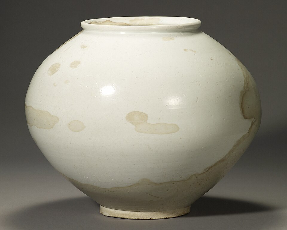 A white rounded ceramic jar photographed against a dark neutral background.