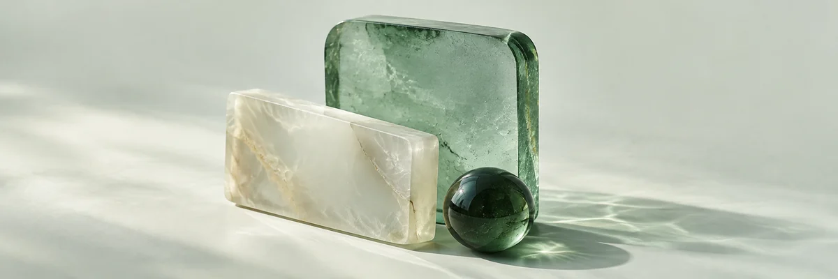 Frosted green glass and an opalescent ivory slab with a polished green sphere, casting soft shadows and caustic light.