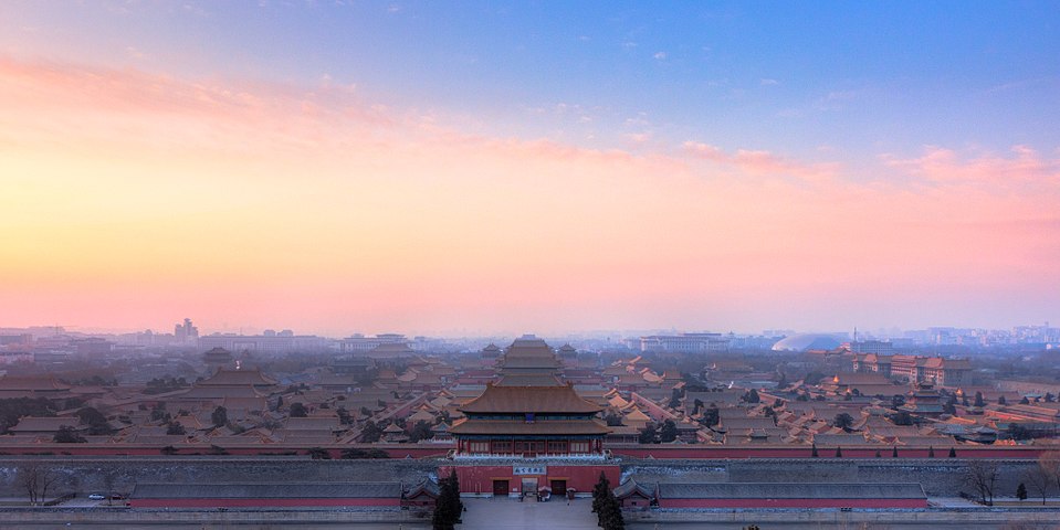 Palace roofs and courtyards of the Forbidden City under a pink evening sky.