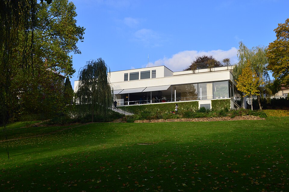 White modernist Villa Tugendhat seen across a lawn beneath trees.