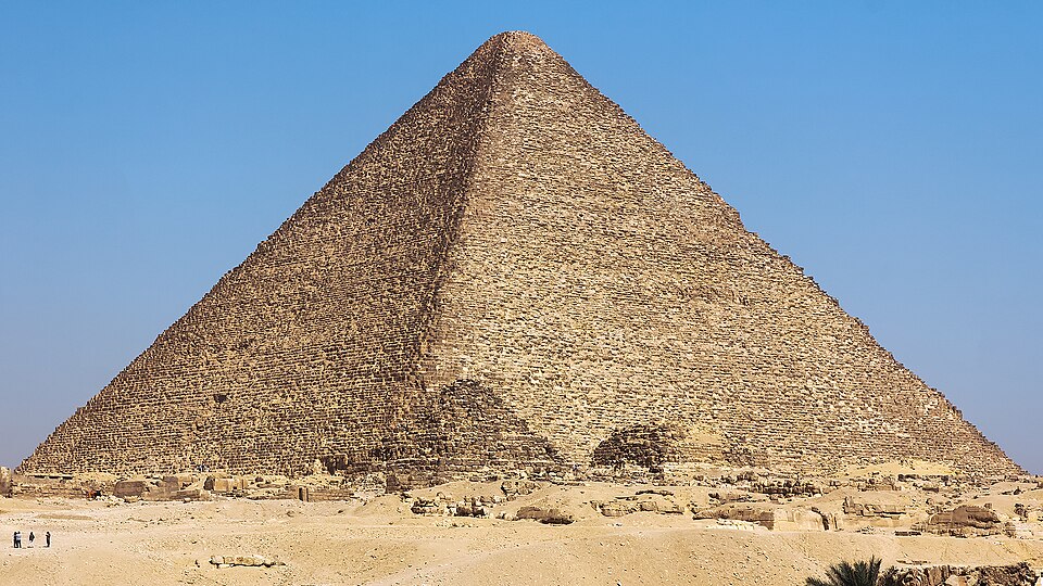 Stone pyramid at Giza against blue sky, seen from the desert floor.