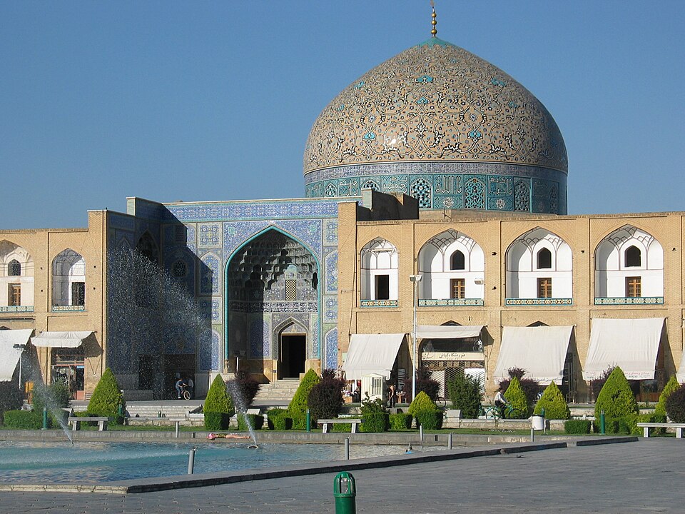 Tiled mosque dome and arched facade facing a public square.