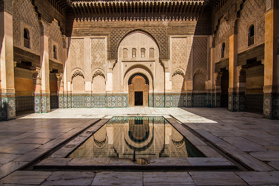 Ornamented courtyard with carved wall surfaces, arches and a central rectangular pool.