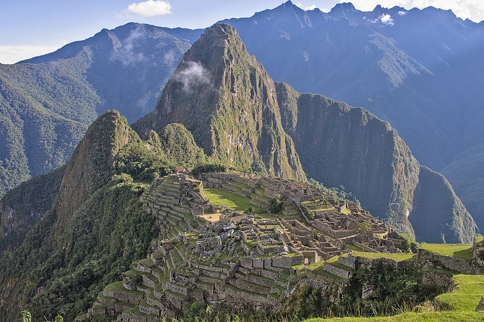 Machu Picchu stone terraces and ruins beneath steep green mountain peaks.